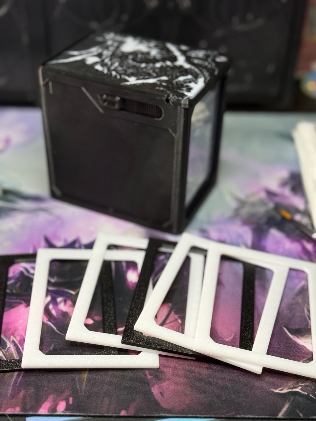 Loose black and white single/sleeve adapter pieces arranged in front of an Alters By Rin deck box.